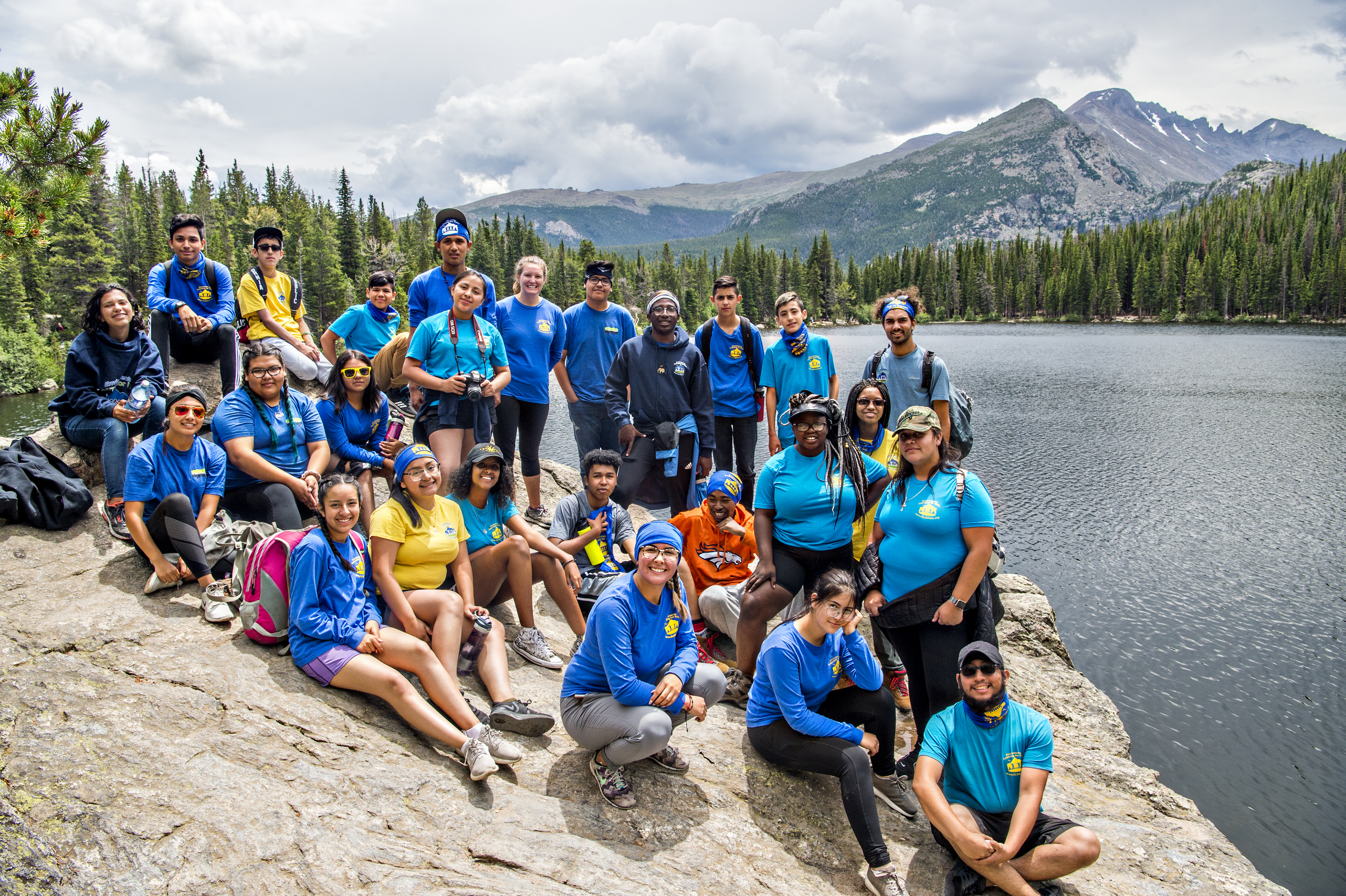 a large group is gathered on a rock in front of a beautiful mountain scene